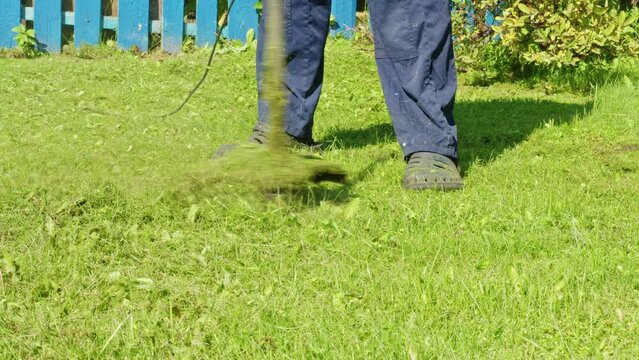 Faceless man in summer sandals mowing lawn with brush cutter. Leg, feet of male yardman in waterproof outdoor slippers who holds lawnmower. Gardener working on grassplot, backyard with grass trimmer