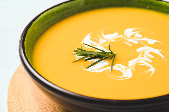 Closeup Of Pumpkin Cream Soup Garnished With Heavy Cream And Rosemary. Thick Butternut Squash Bisque In Green Bowl On Wooden Tray. Selective Focus