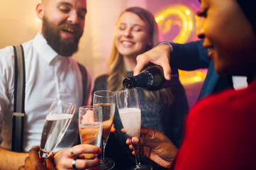People hands holding flute glasses while pouring champagne