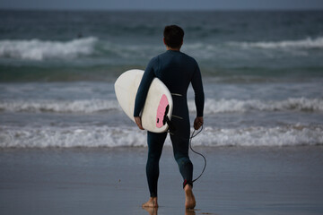 A surfer with a green wetsuit and a white surfboard on A Lanzada beach, O Grove, Pontevedra, Galicia