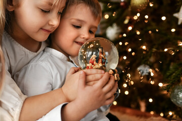 The kids looking at a christmas glass ball with a nativity scene of the birth of Jesus Christ