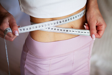 Slim young woman measuring her thin waist with a tape measure at home