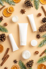 Winter skin care concept. Top view vertical photo of cosmetic bottles fir branches in frost dried orange slices pine cones anise and cinnamon sticks on isolated beige background with copyspace