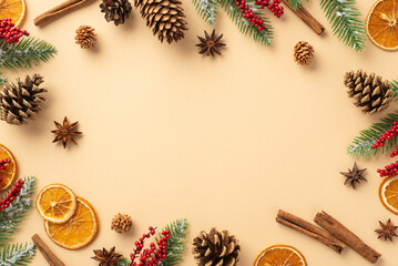 Winter holidays concept. Top view photo of spruce branches in hoarfrost mistletoe berries dried orange slices pine cones and cinnamon sticks on isolated beige background with copyspace in the middle