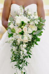 Close up of woman in wedding dress, holding beautiful flower composition with green leaves