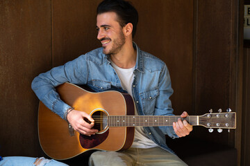 Obraz premium Handsome bearded young man plays guitar smiles and looks away leisure activity
