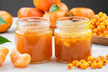 Jars of healthy sea buckthorn and tangerine jam. Plate of sea buckthorn berries and mandarin oranges fruits on background.
