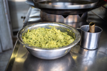 Yellow and Green Falafel Mix in a Silver Stainless Bowl on a Counter in a .Restaurant by Large Pan Filled with Boiling Oil in Close-Up Shot