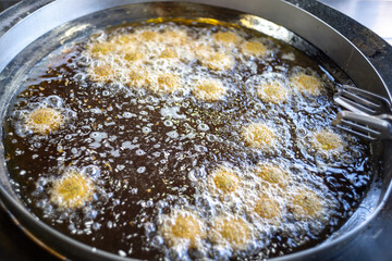 Clamp by the Side of a Dozens of Golden Falafels Frying in a Large Pan Filled with Boiling Oil in Close-Up Shot
