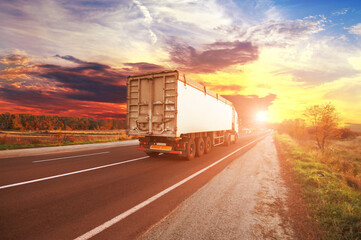 Truck with a trailer on the countryside road against sky with sunset - 544198541
