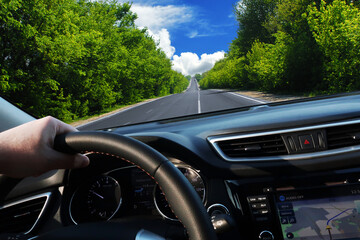 Car dashboard with driver's hand on the steering wheel and road against a sky with clouds - 544198596