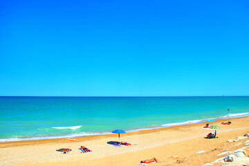 Relaxing scenery in Porto Potenza Picena with a sandy beach, white rocks, colored parasols, people enjoying the sun and the azure turquoise waters of the Adriatic Sea under a blue summer sky
