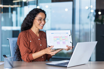 Portrait successful businesswoman, Latin American woman shows a report of financial documents online interlocutors in the laptop screen, an employee inside an office building online video conference.