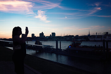 Girl Silhouete making selfie infront of Hamburg from the theater harbor side , where the sunset is...