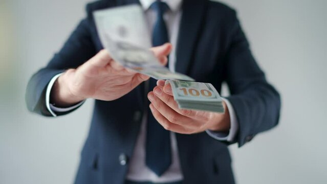 Formally dressed man makes money rain from US dollar bills. Slow motion.