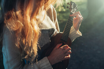 Young beautiful woman playing ukulele and singing in autumn park.