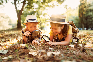 Two little kids with backpacks examining plants through magnifying glass in forest