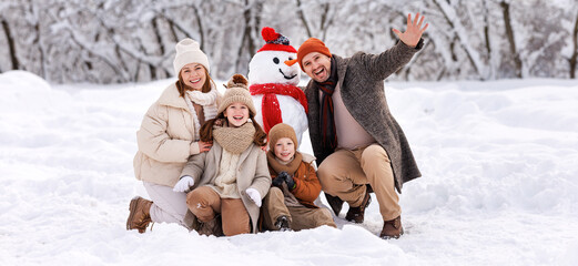 Happy family in warm clothes laughing merrily  while making snowman together