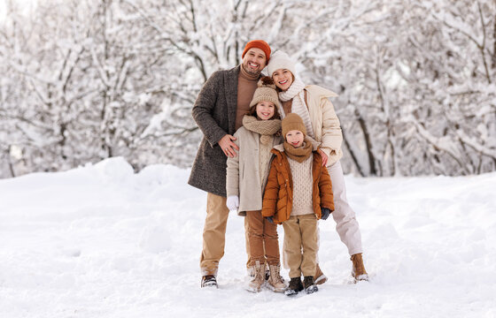 Happy family in warm clothes smiling at camera while playing on fresh air in winter snowy forest