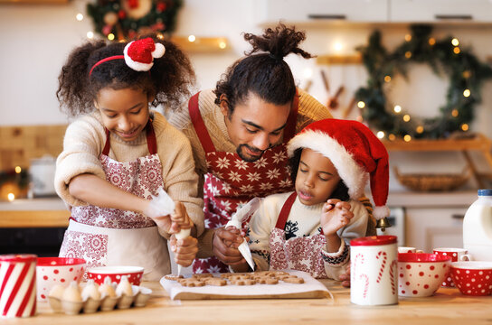 Happy ethnic family father and two kids in festive outfit making Christmas cookies together in kitchen
