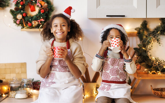 Happy ethnic children on Christmas eve,   girl and boy drink hot cocoa drink that they baked together in cozy kitchen at home