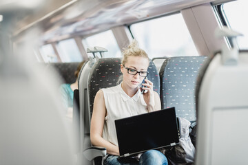 Businesswoman talking on cellphone and working on laptop while traveling by train. Business travel...