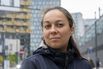 Street portrait of a woman 40-45 years old against a blurred background of modern buildings.