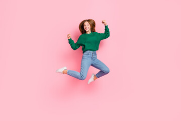Full length photo of excited lucky young lady wear green sweater jumping high rising fists isolated pink color background
