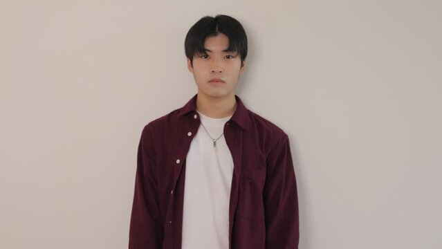 Asian boy standing still against the white wall.