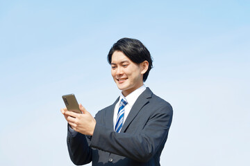 スマホを使うビジネスマン　青空背景