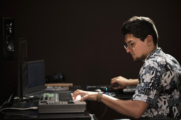 latin man using audio equipment and playing on a keyboard in a home recording studio