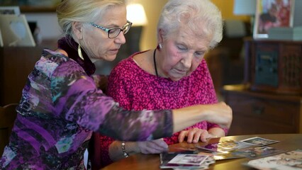 Closeup of senior elderly smiling woman looking at old photos and remembering memories with daughter at the dining room table.