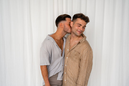Beautiful Gay couple kiss on neck with white curtain background