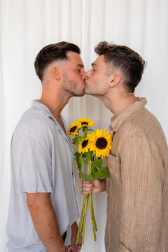Beautiful Gay couple kissing over sunflowers with white curtain background