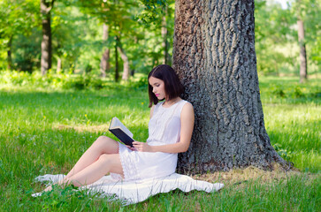 Young woman sitting in the forest and reading book on a beautiful summer day
