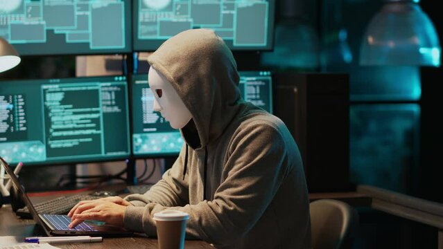 Cyber terrorist with mask hacking database servers, hacker with hood on hacking computer system and activating virus to create malware. Impostor stealing big data, leak information.