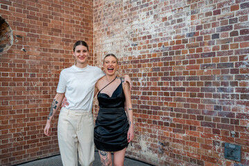 lesbian couple laughing in front of brick wall 