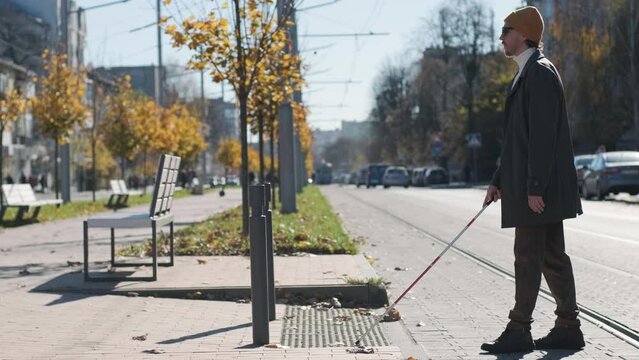 Lone blind man detecting tactile tiles, walking to pedestrian crossing safe road