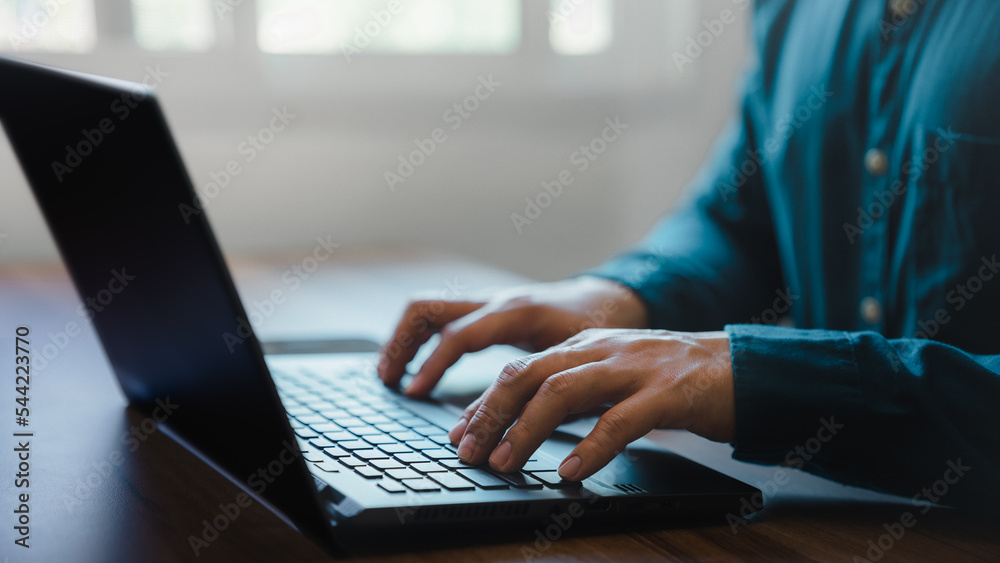 Aufkleber Closeup image of a young man working and typing on laptop computer keyboard on wooden table in cafe.