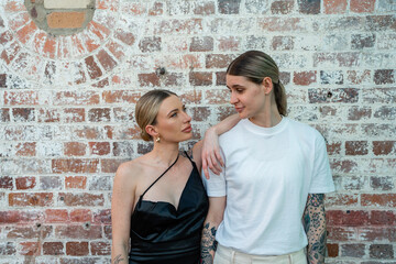 cool lesbian couple serious in front of brick wall looking at each other 