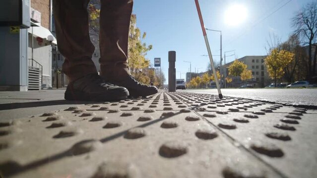 Lone blind man detecting tactile tiles, walking to pedestrian crossing safe road