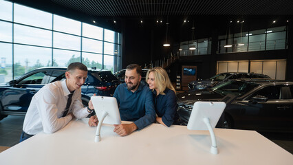 Caucasian married couple chooses a car in a car dealership on digital tablets. 