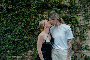lesbian couple kissing in front of city greenery 