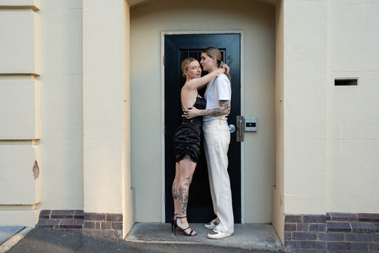 cool lesbian couple kissing on forehead in doorway on street 