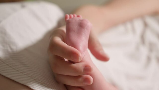 A woman's hand gently touches the legs of a newborn baby taken close-up.