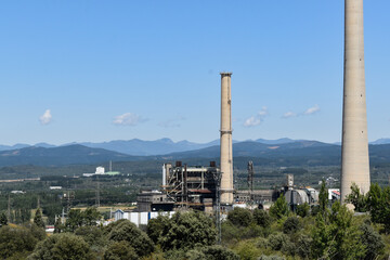 Fototapeta na wymiar Central eléctrica produce energia, de fondo montañas y paisaje verde con un cielo azul claro. 