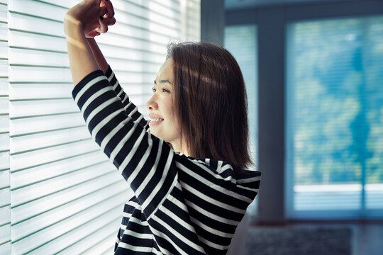 部屋のブラインドを開けストレッチをする女性