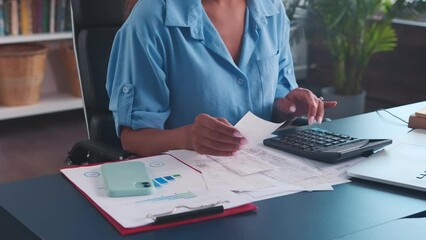 Close-up of female auditor's hand counting expenses of company employees using calculator and cashier's checks to prepare financial report on costs for manager sits at table in office