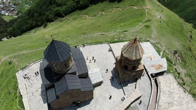 Tourists visiting Gergeti Trinity Church, close up aerial ascend view