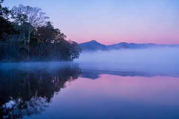 湖面に朝靄の漂う早朝の湖。日本の北海道の屈斜路湖。